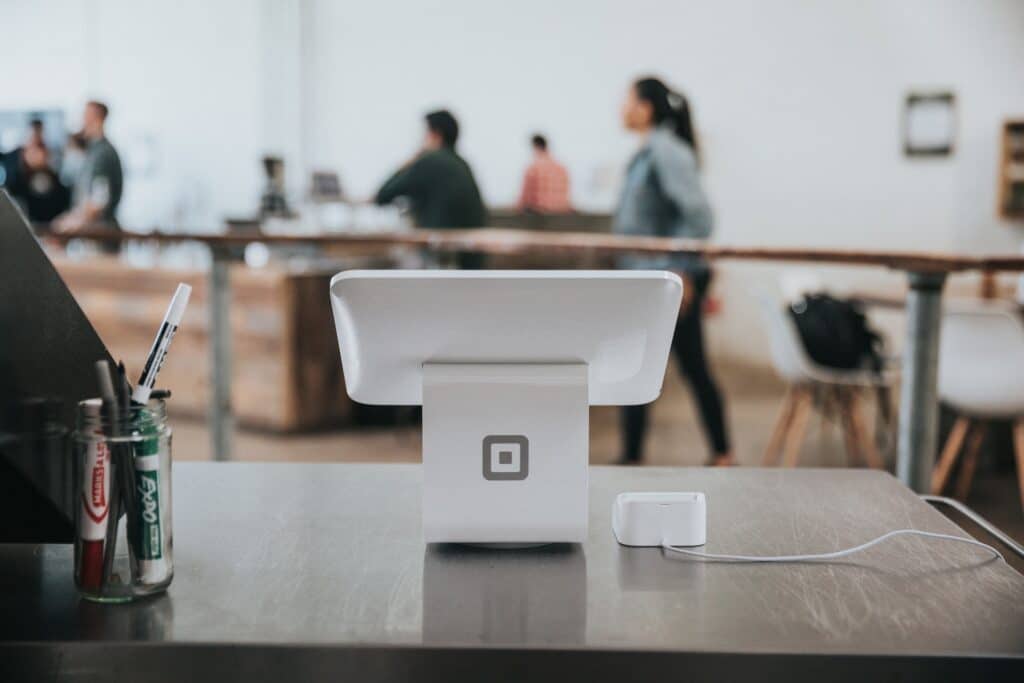 A credit card reader and point of sale pay pad sit on a desk. In the background shoppers and are blurred. Market analysis software can help BNPL services gain valuable insights.