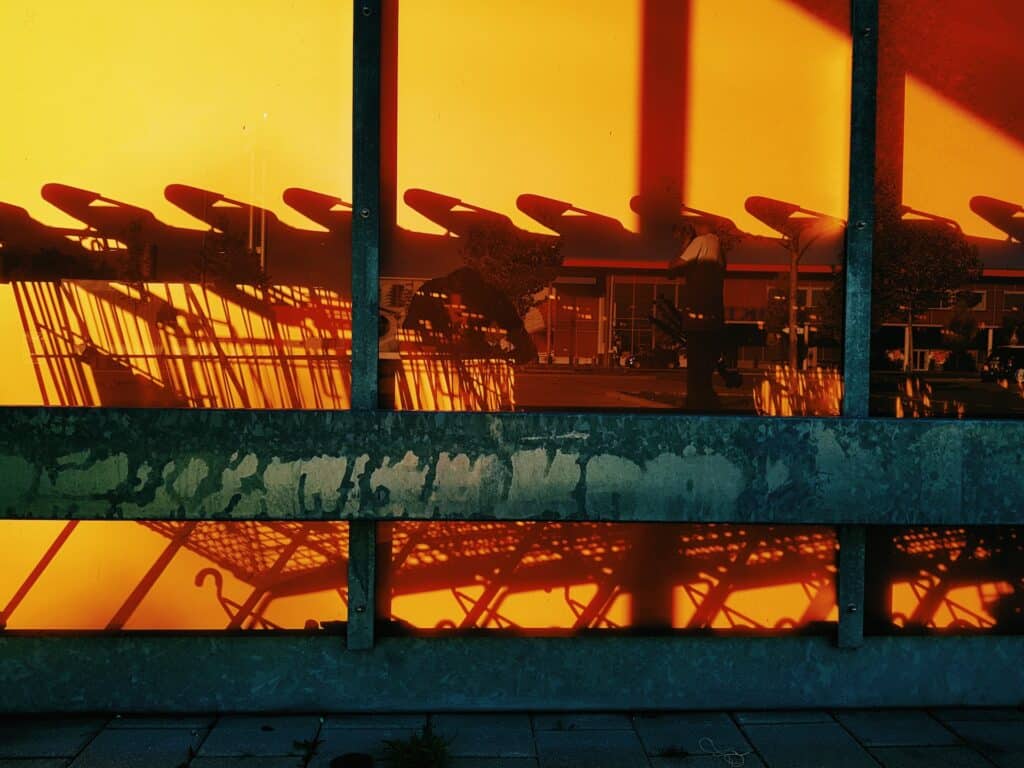 The shadows of shopping carts form a visual pattern against a wall with orange lighting, likely cast from a sunset. Market basket analysis allows retailers to identify shopping behaviors and patterns.
